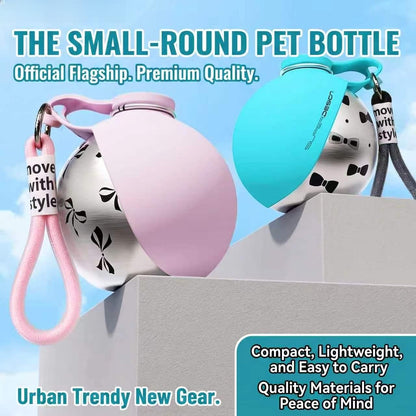 Two small pet water bottles with flip-top lids are shown on a gray pedestal against a light blue sky background. One bottle has a pink flip-top cover and a pink wrist strap, and the other has a turquoise flip-top cover and a dark gray wrist strap.