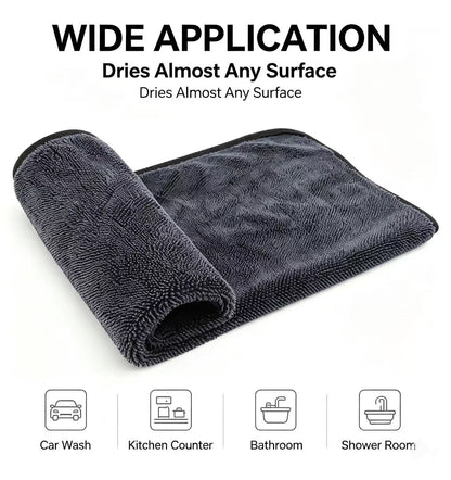 A dark gray microfiber drying towel shown rolled and partially unrolled on a white background, with text reading 'WIDE APPLICATION' and small icons for car wash, kitchen counter, bathroom, and shower room.